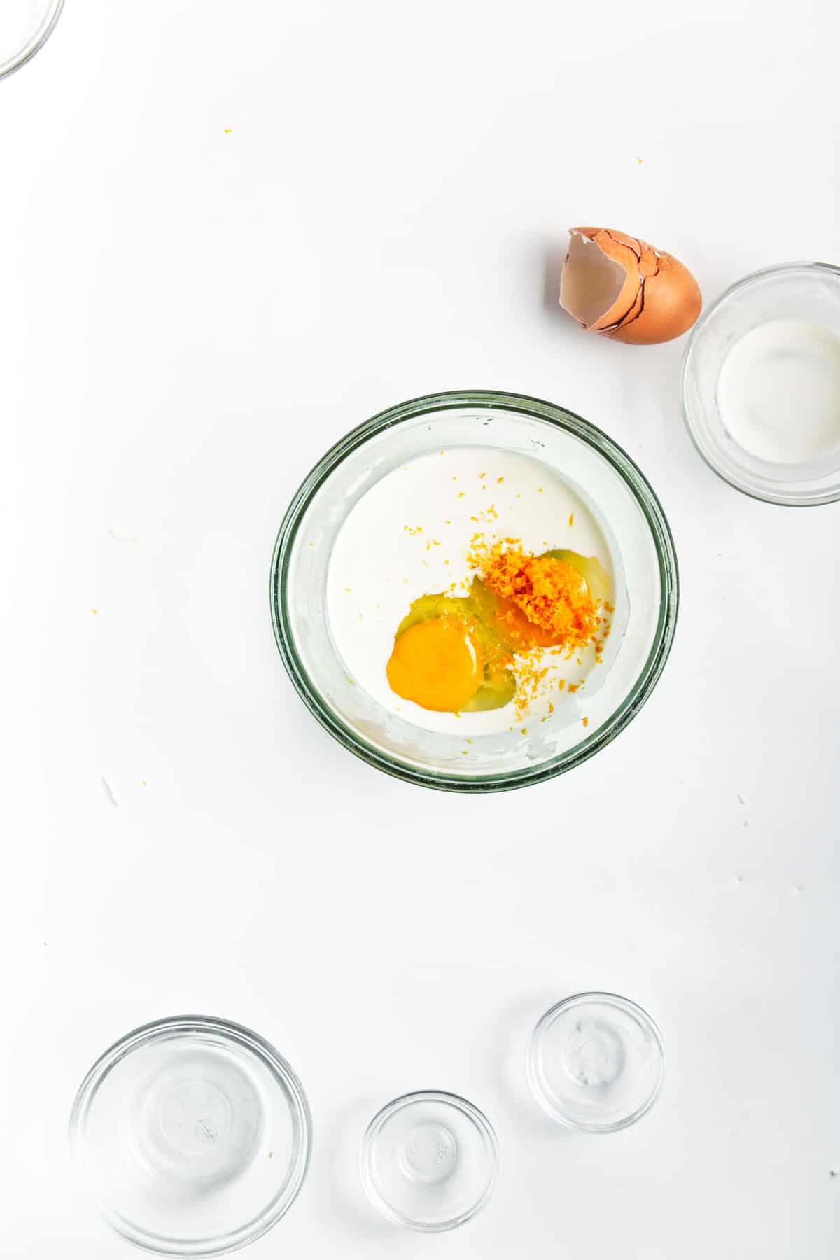 Eggs, cream, and orange zest in glass bowl.