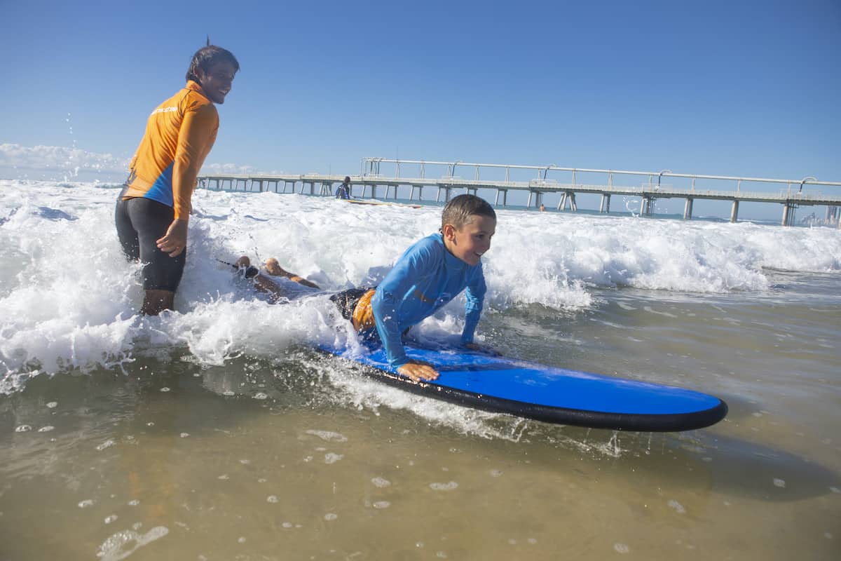 Child learning to surf on blue surfboard with instructor.