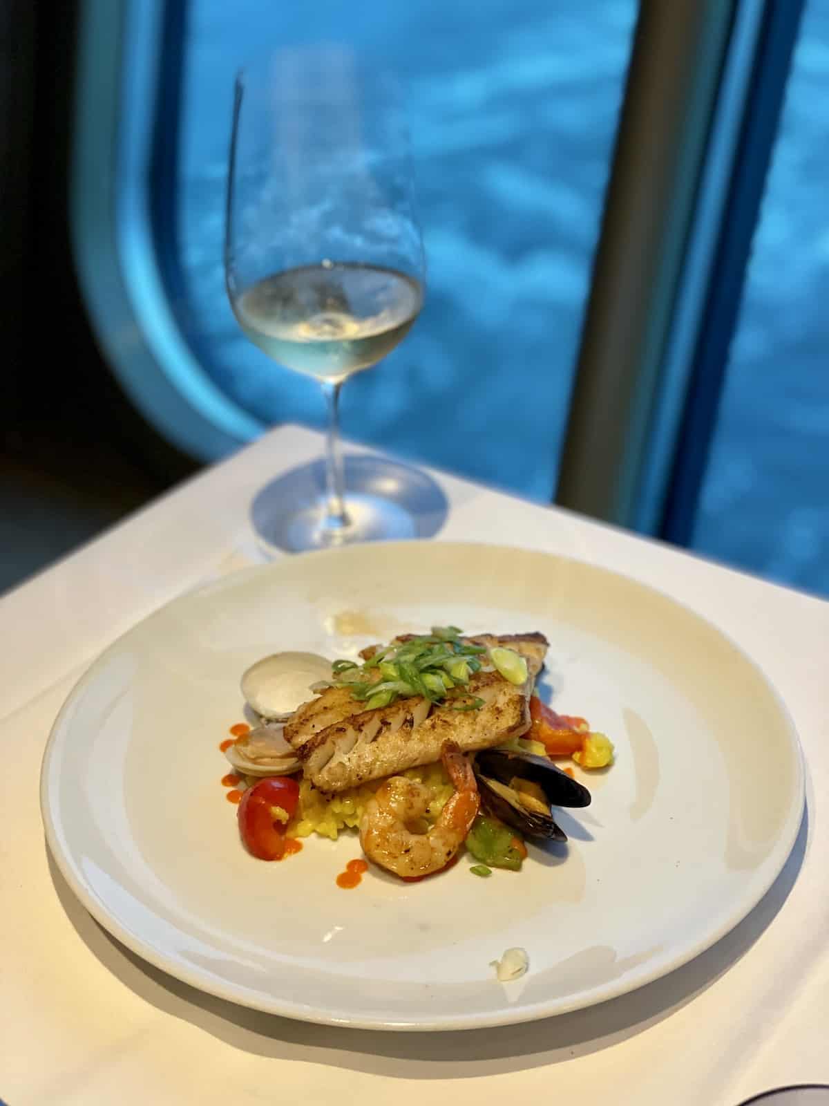 Fish, shrimp, mussells, and clams with vegetables on a white plate.