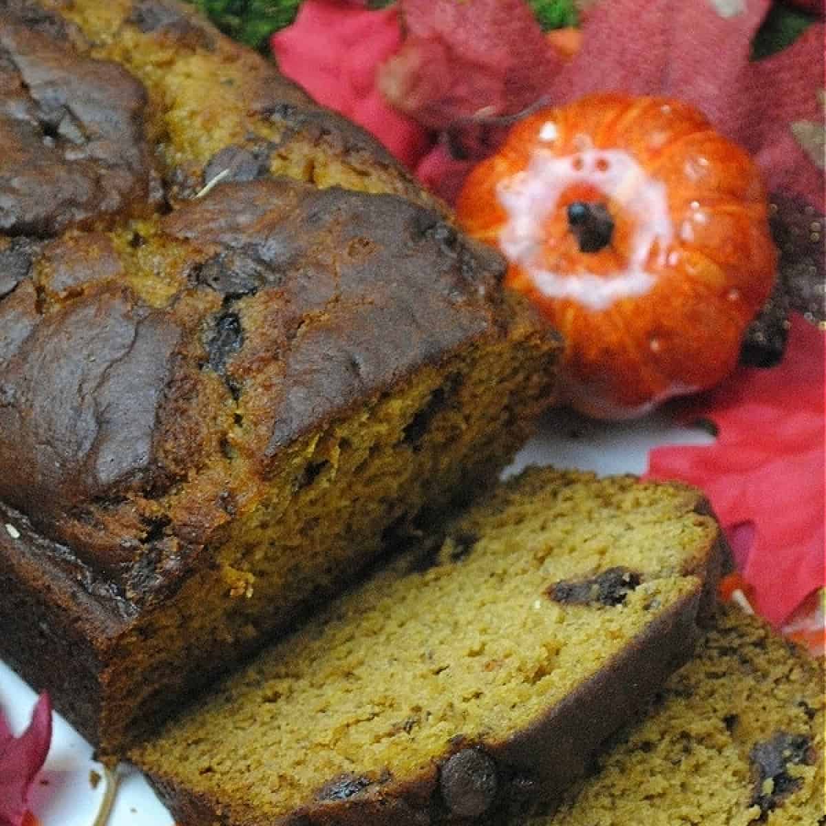 Pumpkin chocolate chip banana bread sliced with fall leaves in background.
