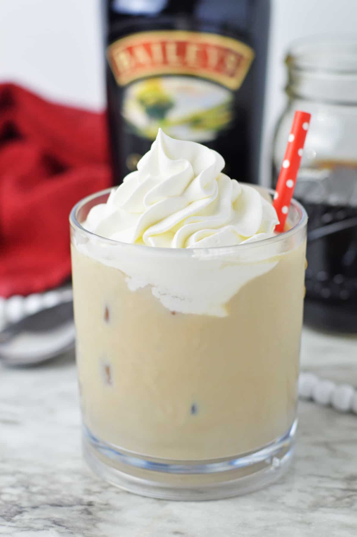 Baileys Iced Coffee with whipped cream and a red straw in a glass.