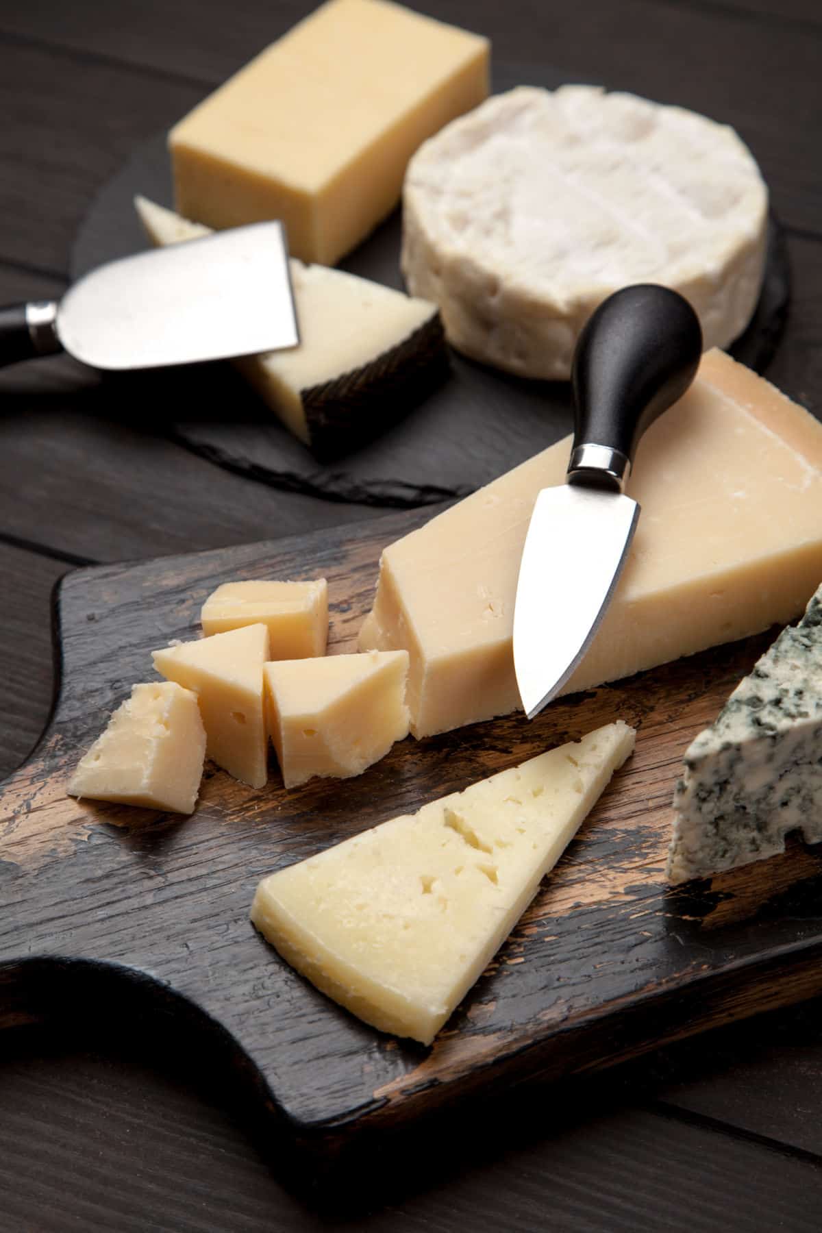 Cheeses on cutting board with cheese knives.