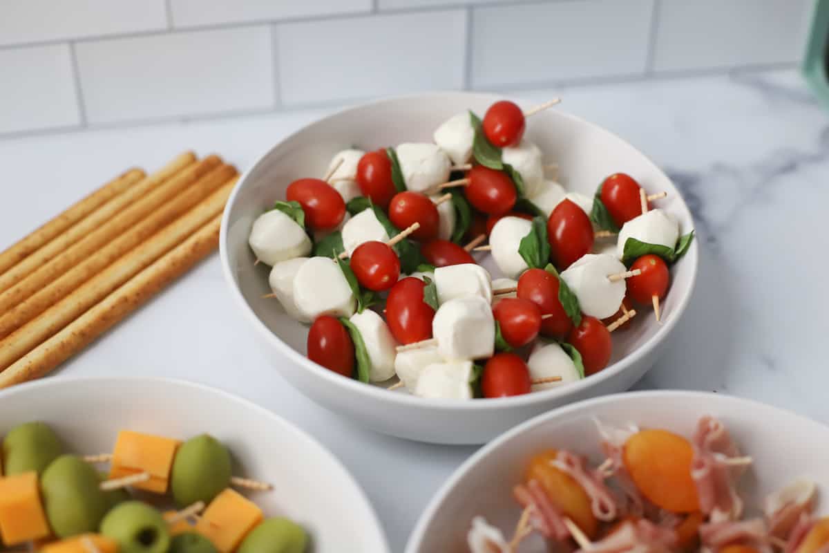 Bowl of cherry tomatoes, fresh mozzarella, and basil on toothpicks.