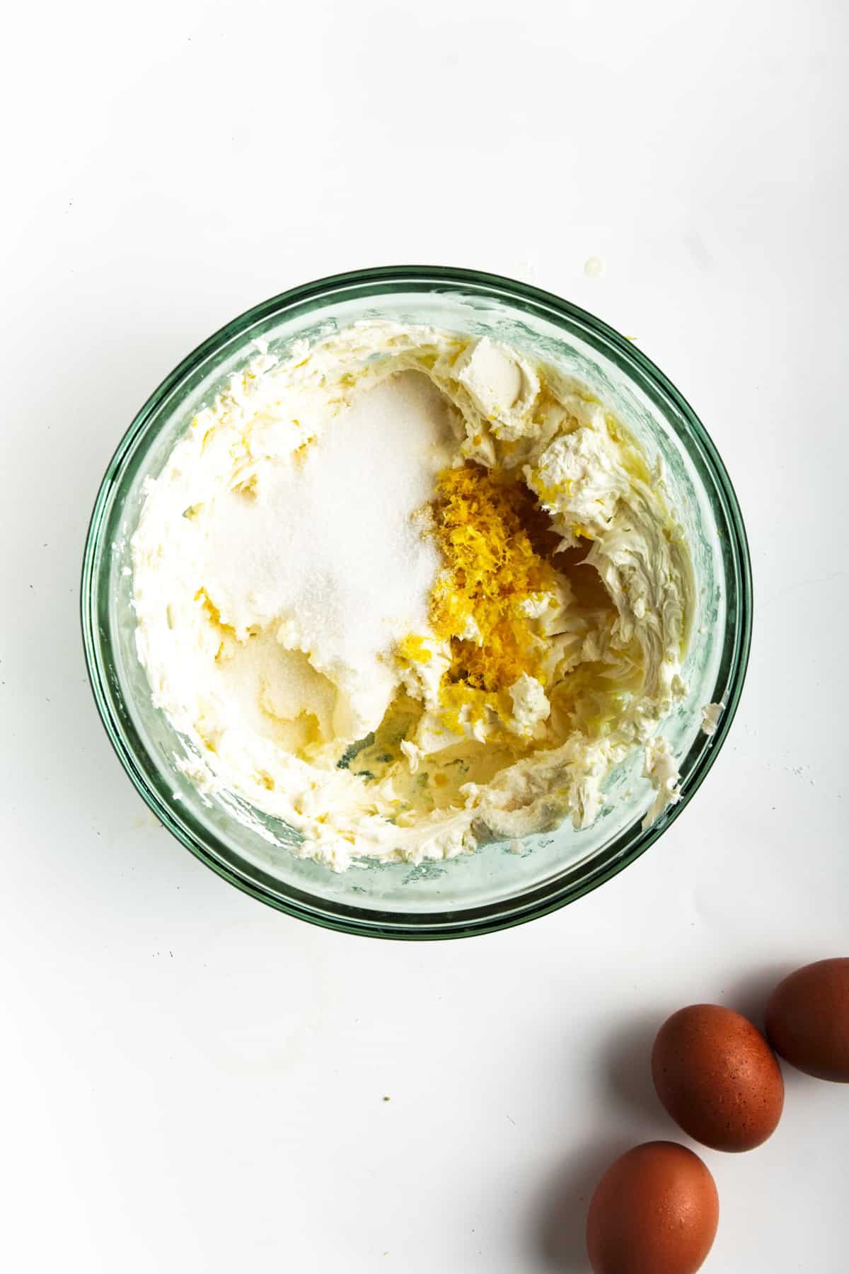 Cream cheese mixture with sugar, lemon zest, and ginger in glass bowl.