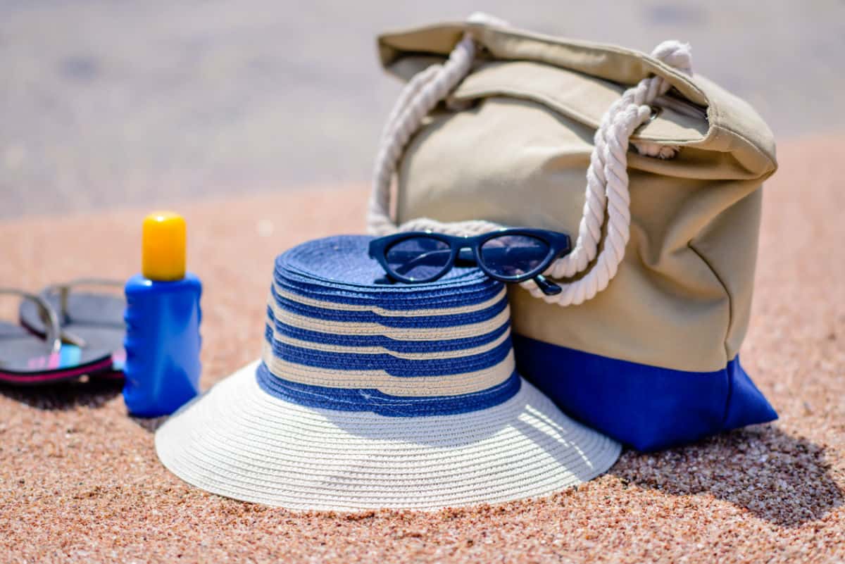 Hat, bag, suntan lotion and flip flops on beach.