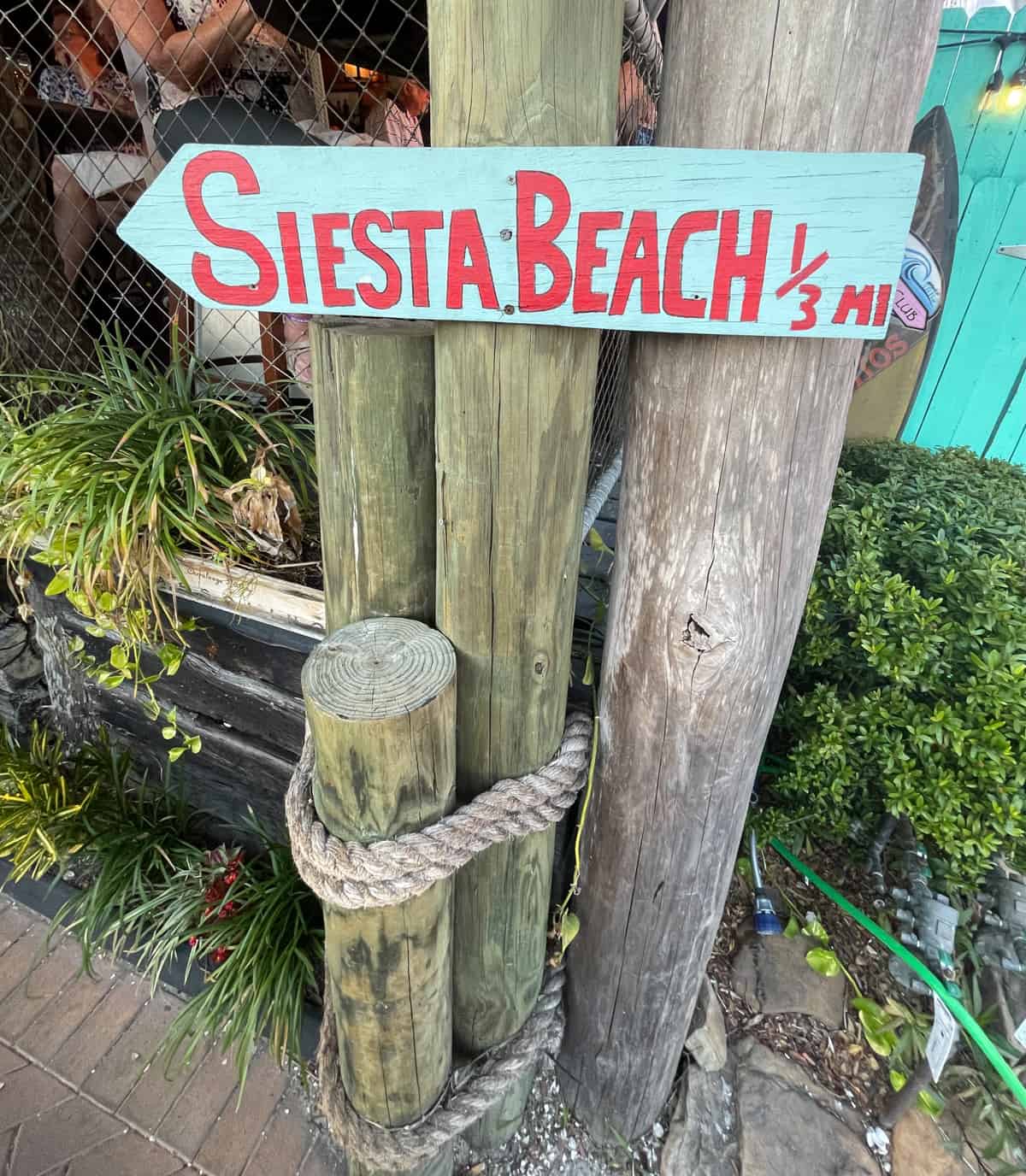 Sign reading Siesta Beach 1/3 mile on wood pole.