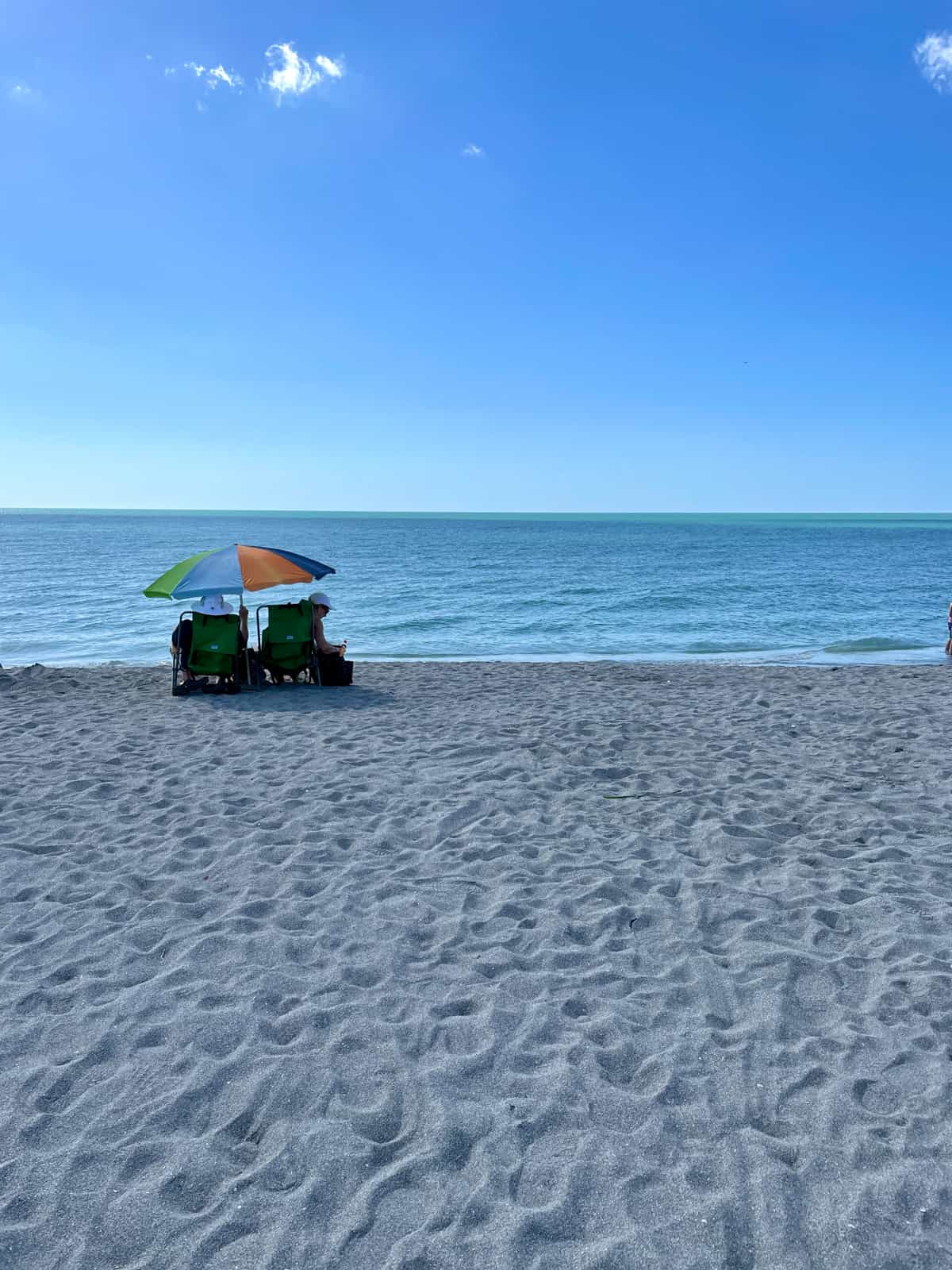 Two people sitting on beach under umbrella.