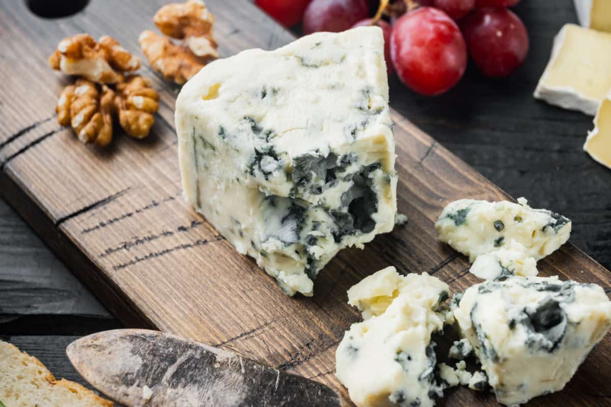Blue cheese on wood board with walnuts and grapes.
