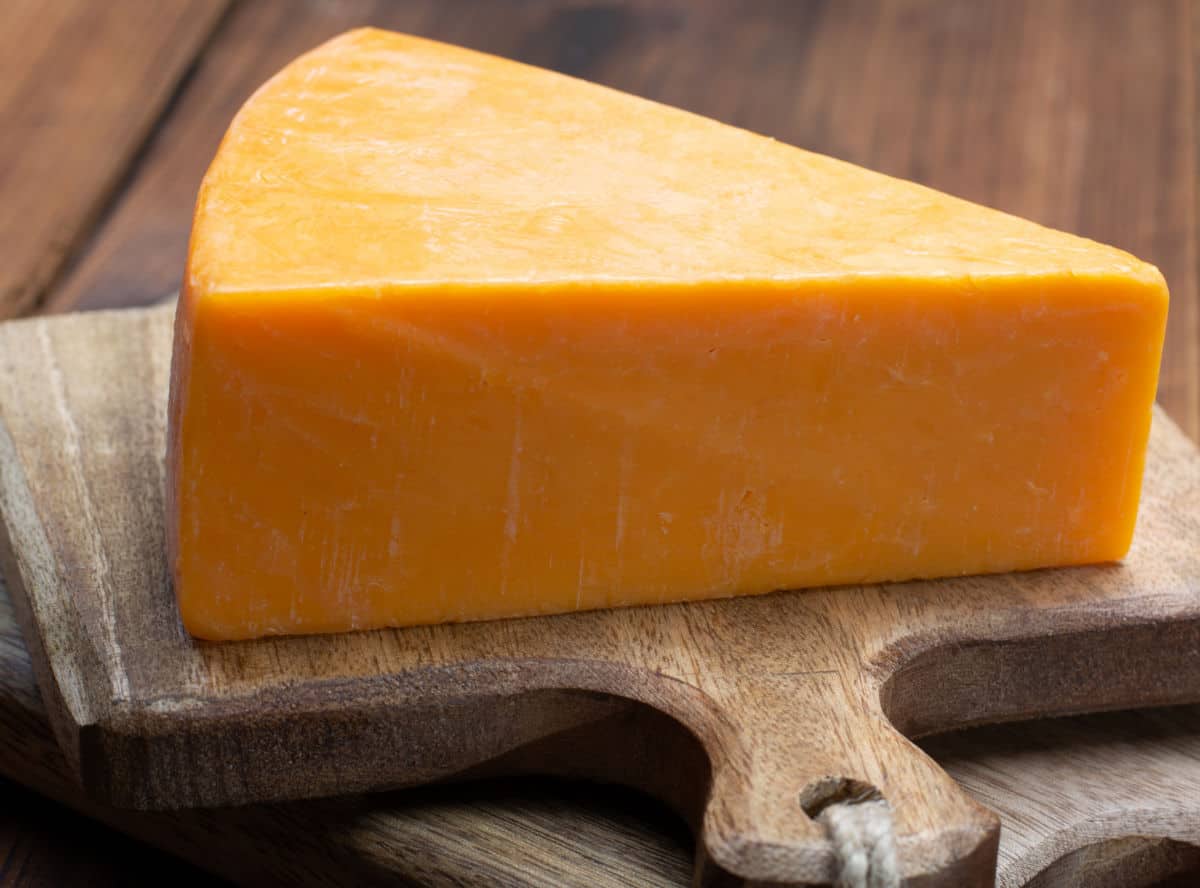 Cheddar cheese wedge on cutting board.