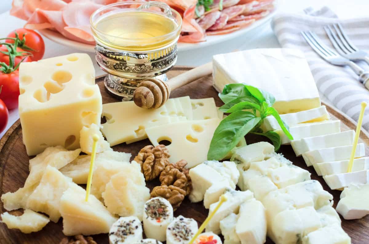 Cheeses and honey with basil and walnuts on wood board.