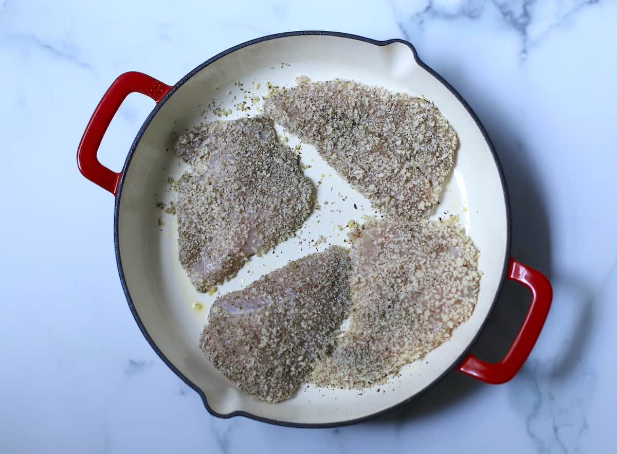 Panko crusted chicken breasts in red skillet.