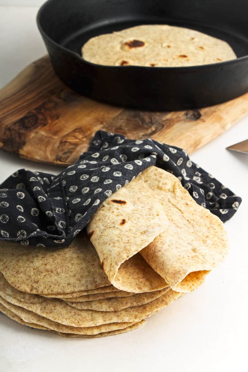 Flour tortillas wrapped in napkin with cast iron skillet behind.