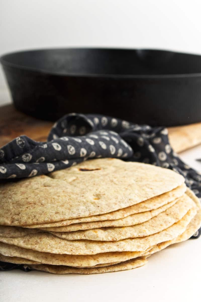 Flour tortillas wrapped in napkin with cast iron skillet behind.