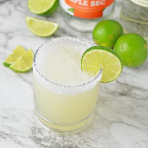 Frozen mezcal margarita on a white counter with limes.