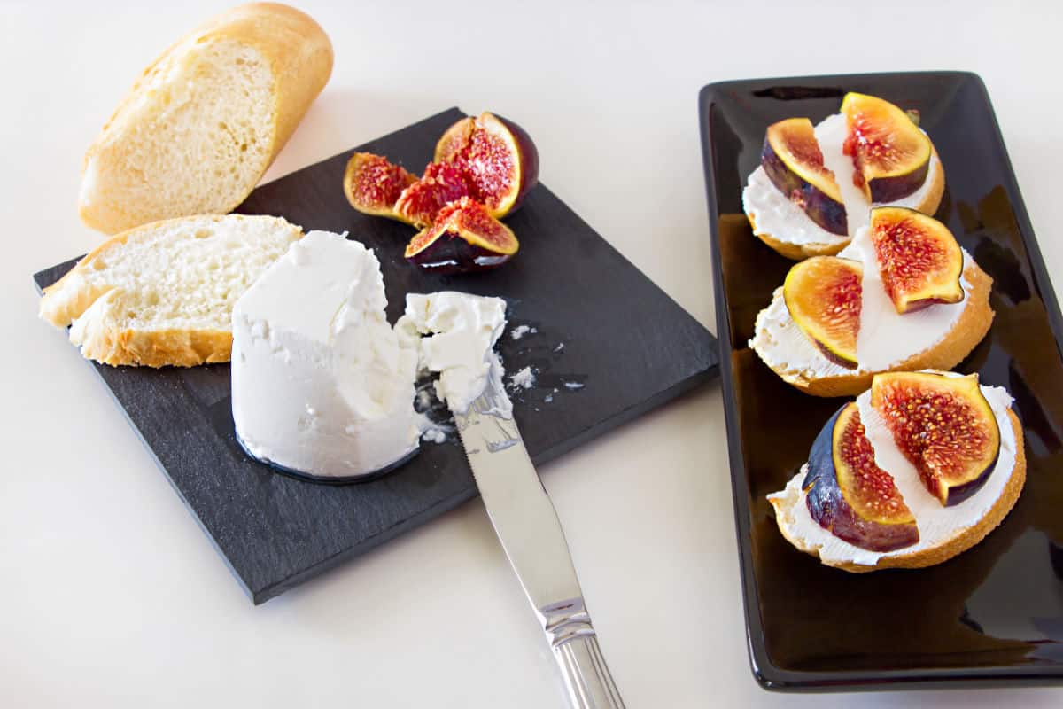 Goat cheese on black cutting board with knife, bread, and fig, and same on additional serving platter.