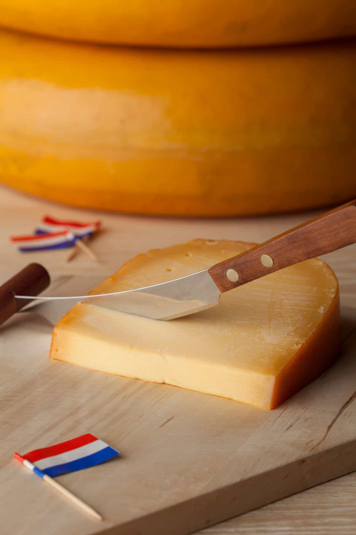 Gouda cheese wedge on cutting board with knife and Netherlands flag.
