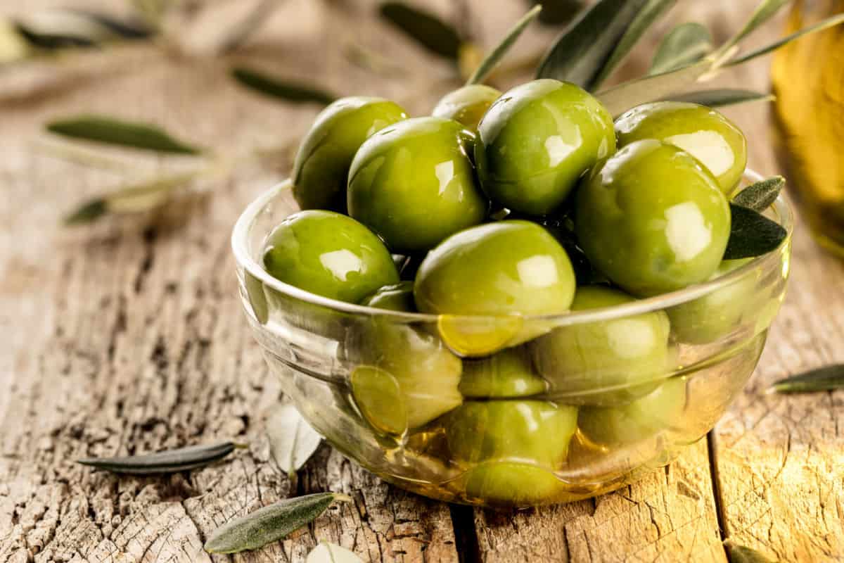 Green olives in oil in a glass bowl.