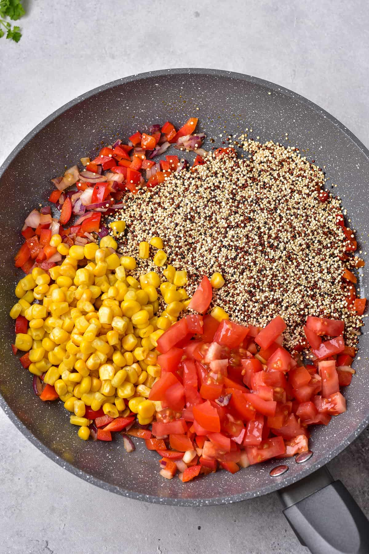 Red pepper, onions, tomatoes, corn, and quinoa in a frying pan.
