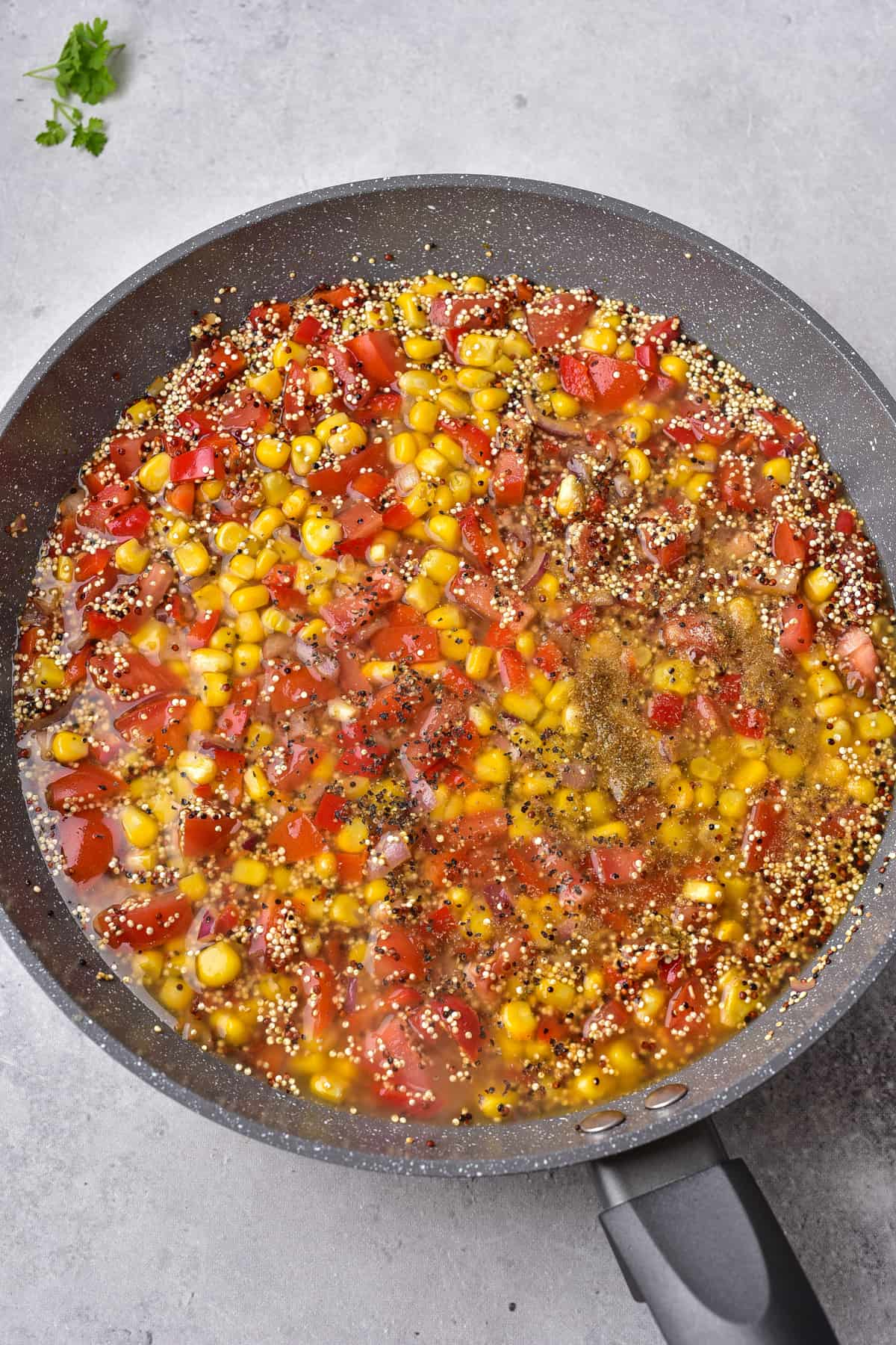 Red pepper, onions, tomatoes, corn, and quinoa with broth in a frying pan.