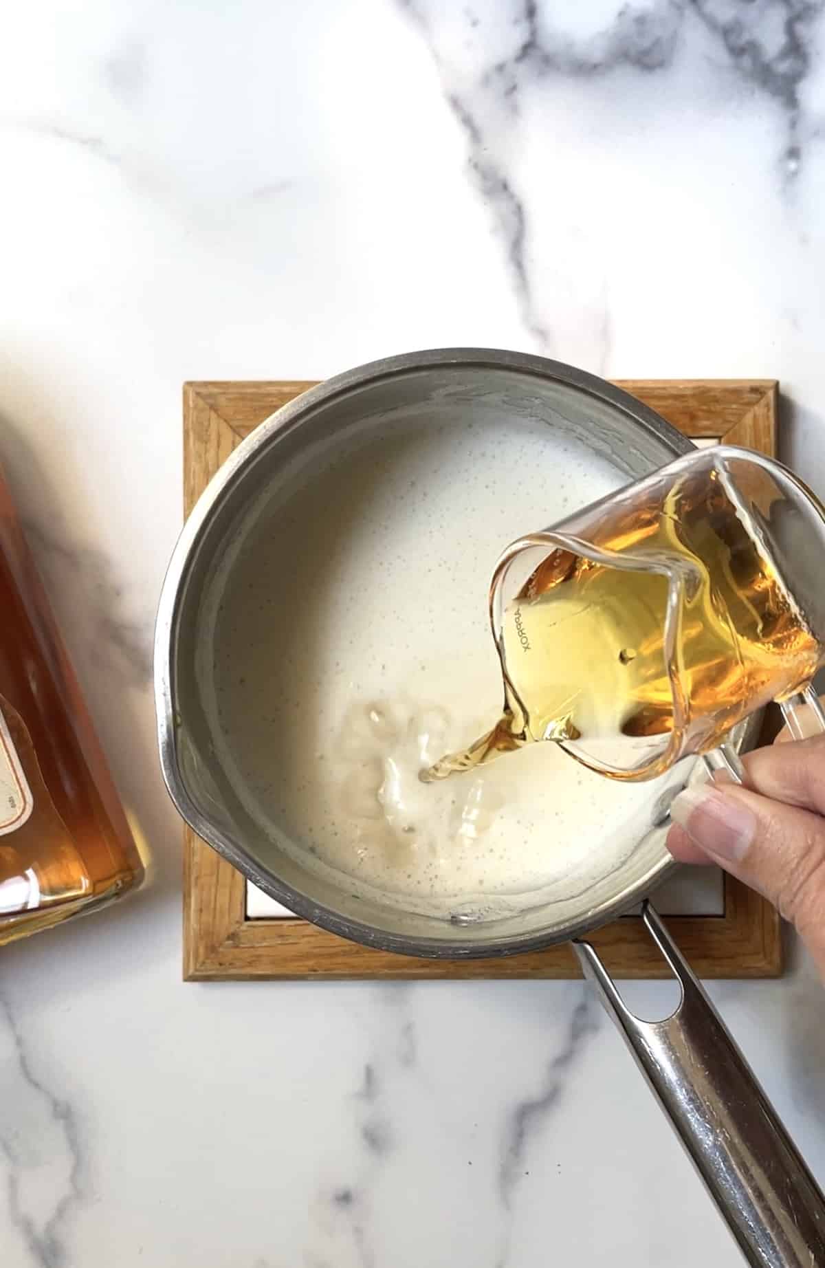 Pouring whiskey into pan of cocktail mixture.