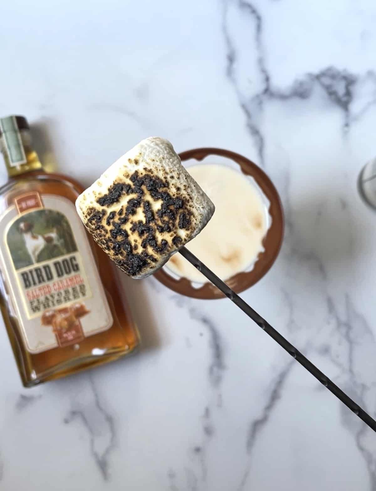 Bird Dog Whiskey bottle with cocktail in a martini glass with a marshmallow over the glass on a skewer.