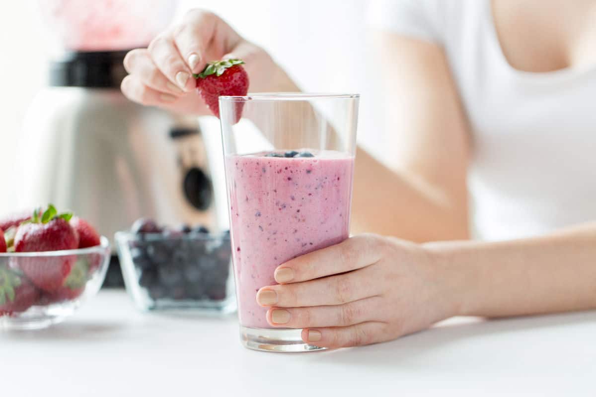 Strawberry milkshake with berries and blender in background.