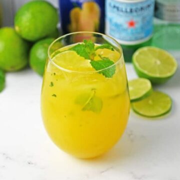 Mango Mojito in a glass with ingredients in background.