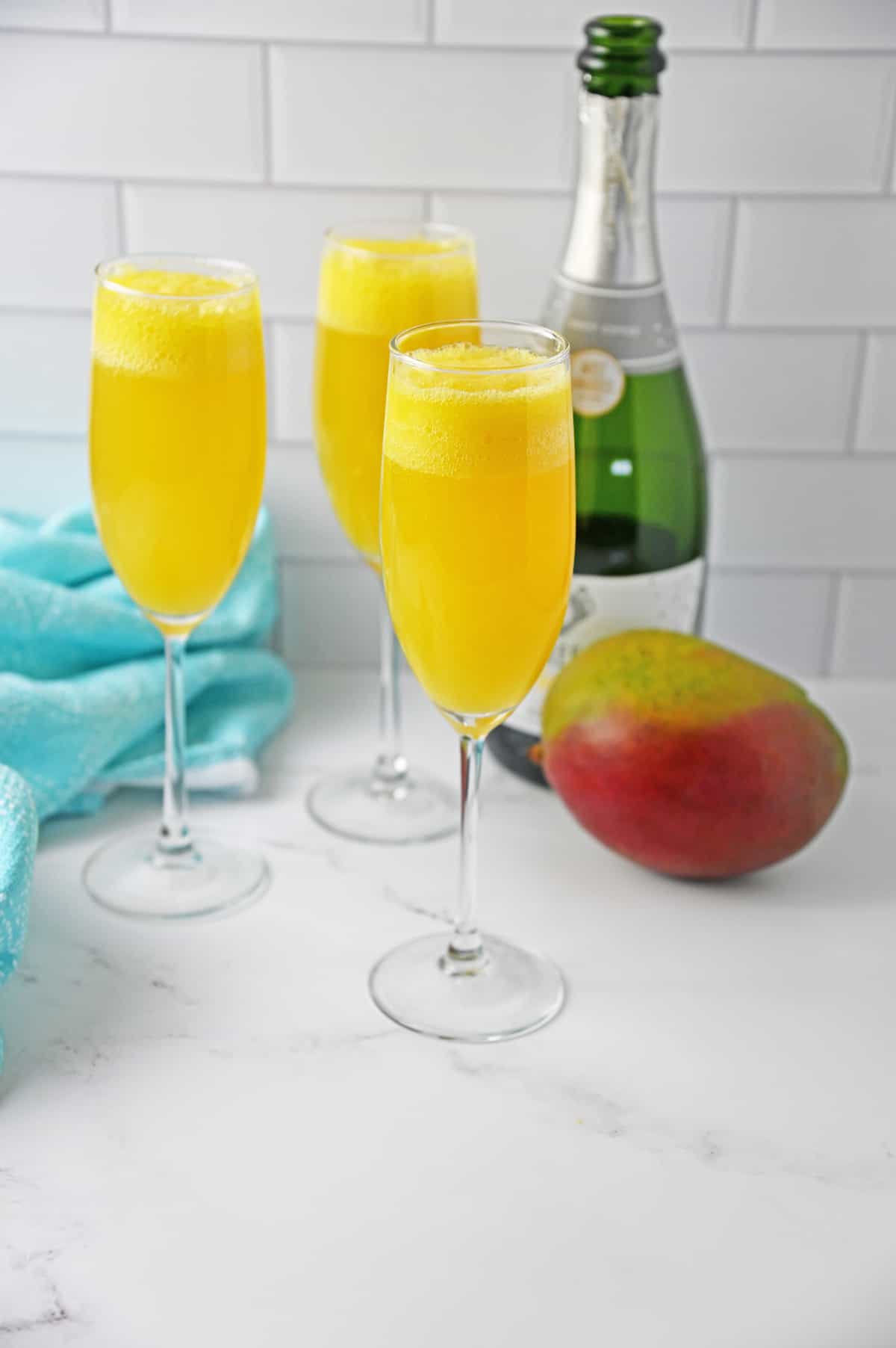 Mango Mojitos with bottle of champagne on white counter with blue napkin.