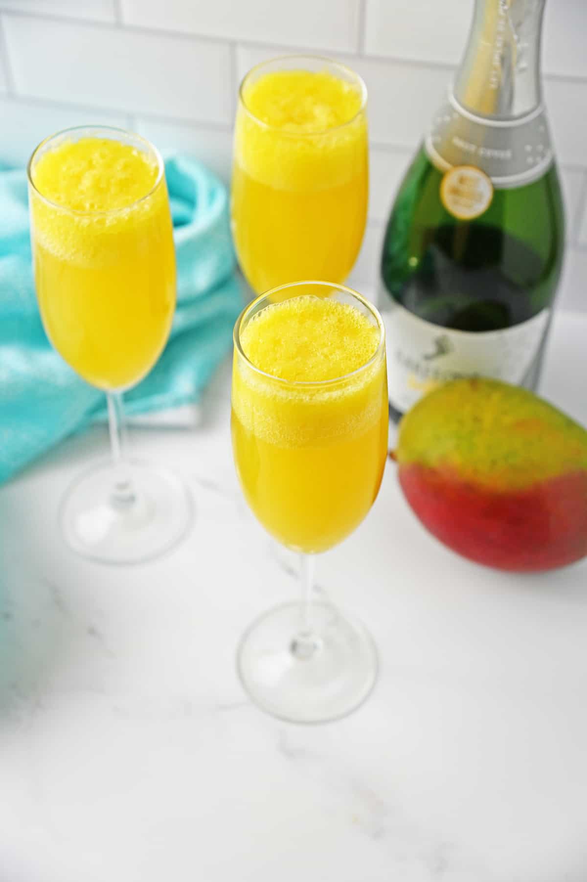 Mango Mojitos with bottle of champagne on white counter with blue napkin.