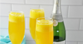 Mango mimosas on white counter with champagne in background.