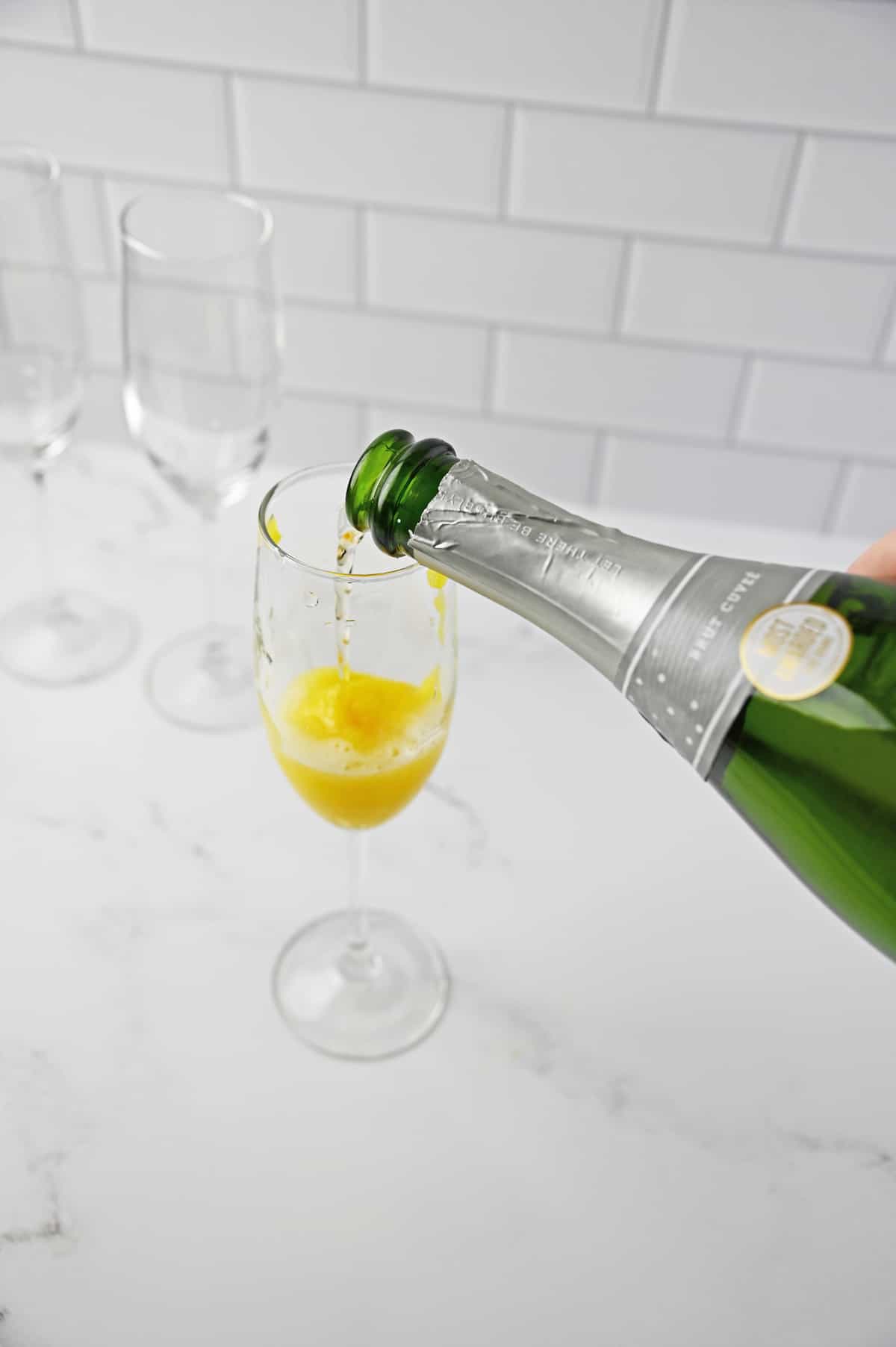 Pouring champagne into flute glass with mango puree.