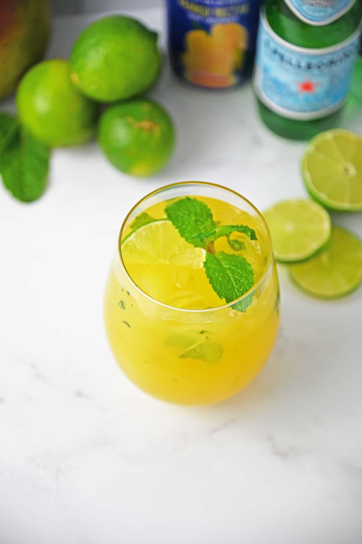 Mango mojito in a glass with mint garnish on a white counter.