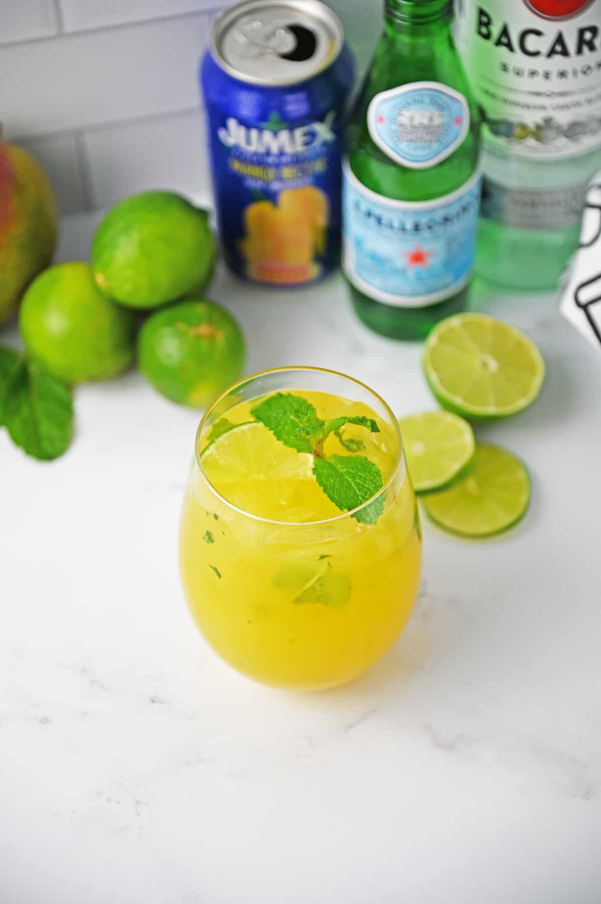Mango mojito in a glass with mint garnish on a white counter.