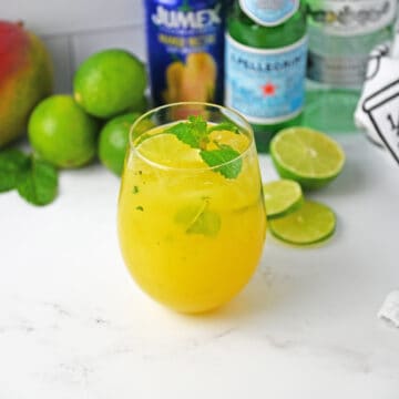 Mango Mojito in a glass with ingredients in background.