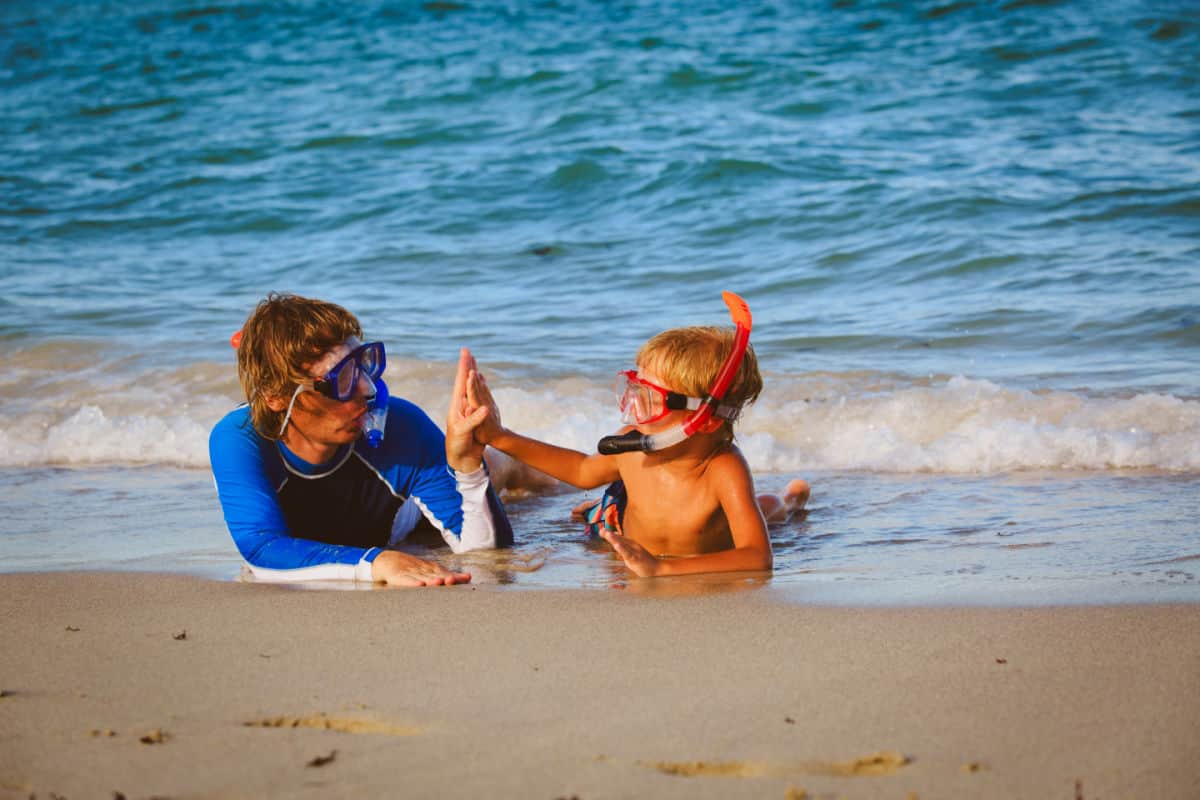 Man and boy laying on sand with snorkels on.