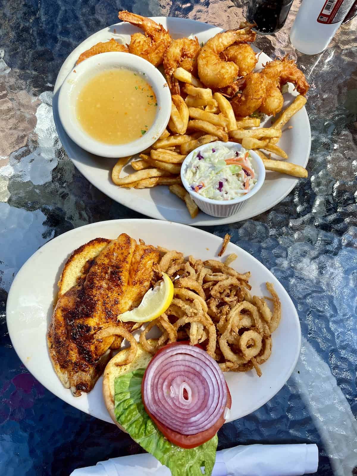 Platter of fried shrimp with French fries and cole slaw and platter of fish sandwich with onion straws.