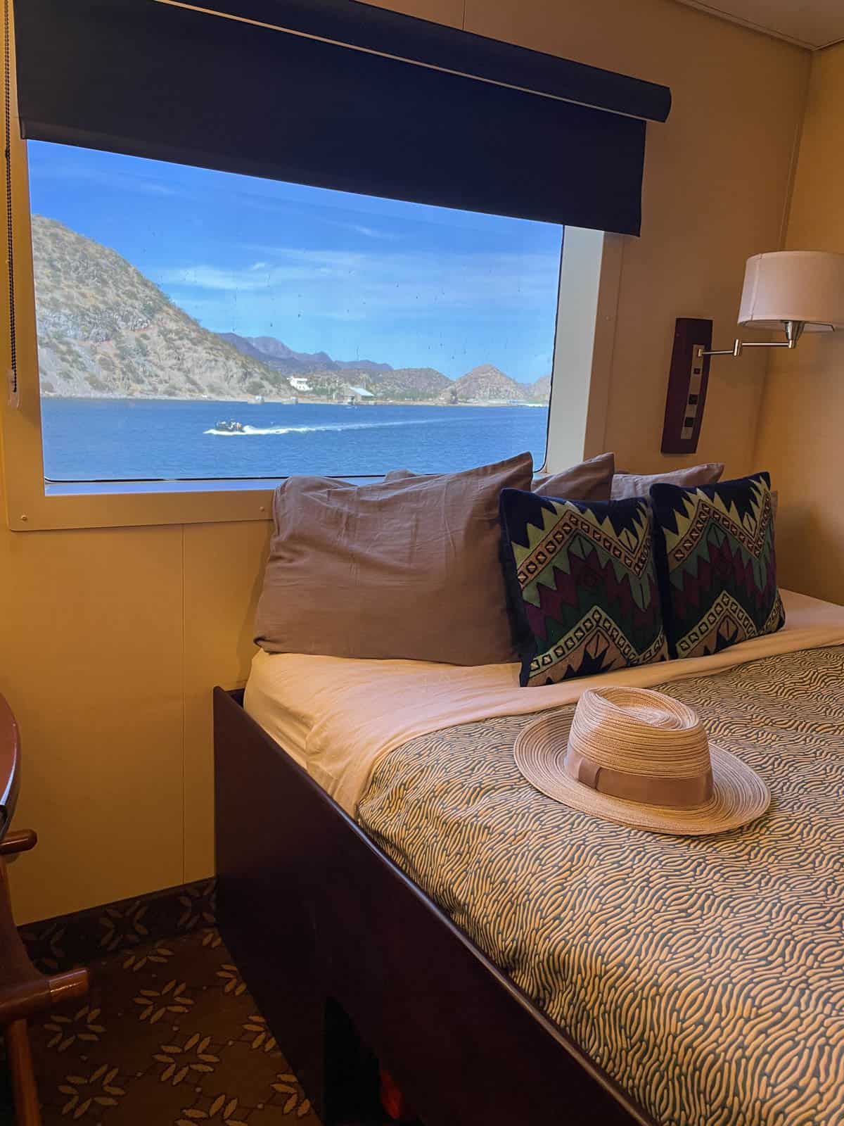 Room on a boat with hat on bed and window looking out at Baja Mexico.