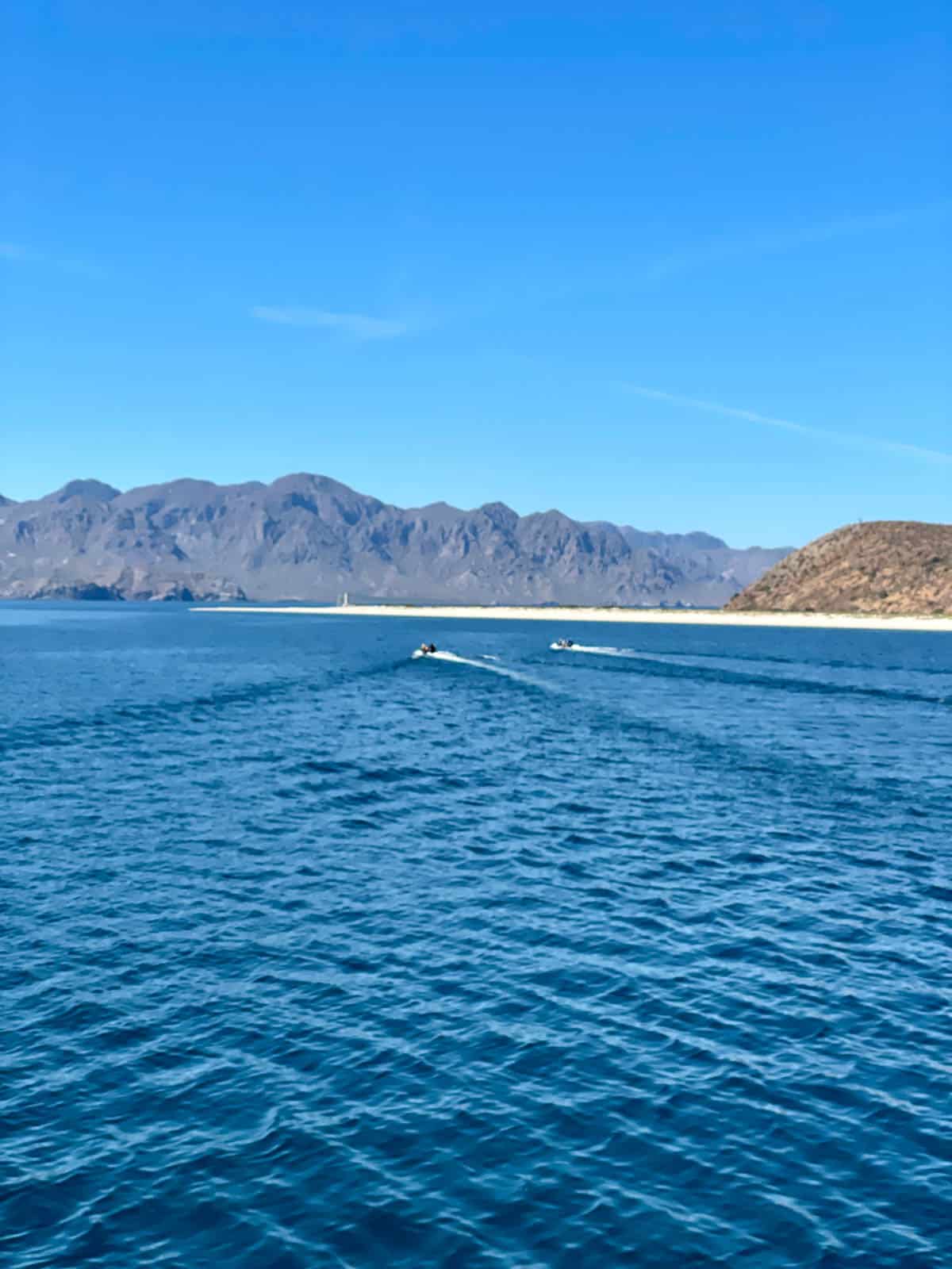 Skiffs heading to shore in Baja Mexico with mountains in background.