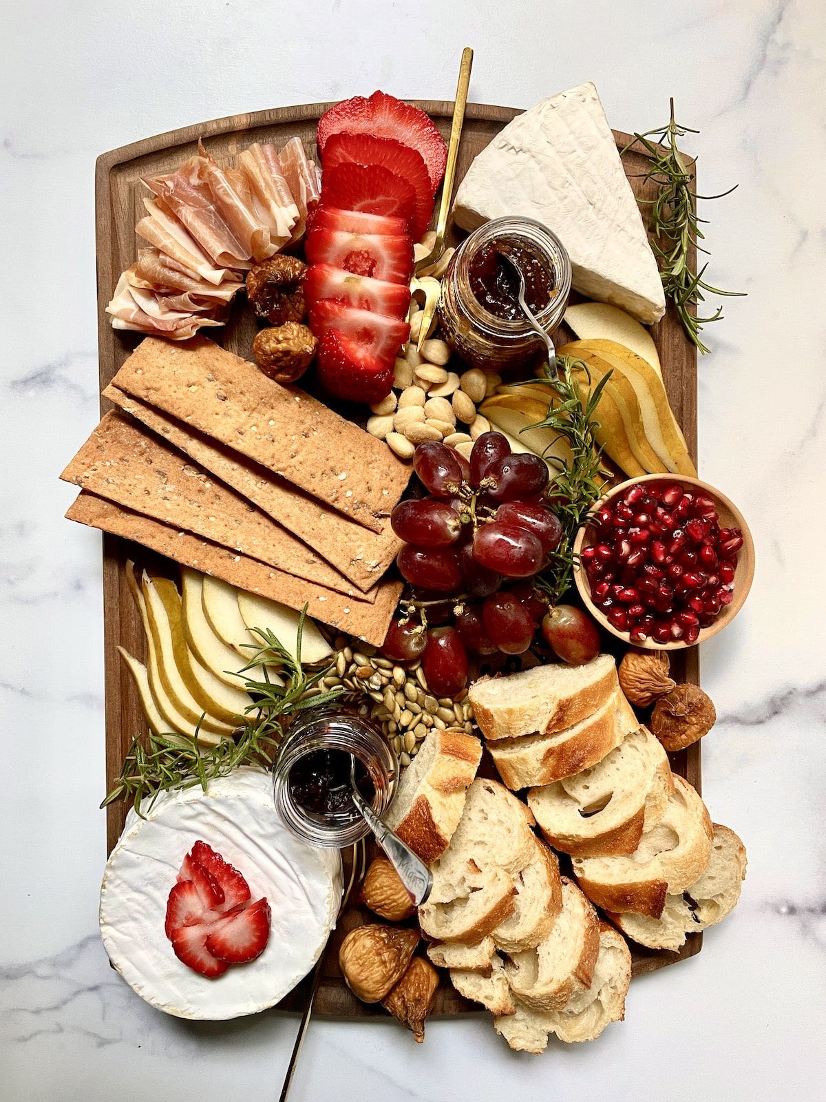 Brie charcuterie board with fruit, nuts, bread, and crackers.