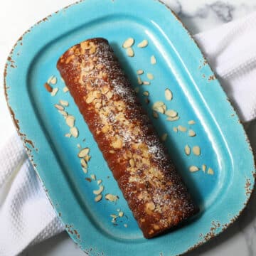Swedish almond cake on blue platter with almonds sprinkled around.