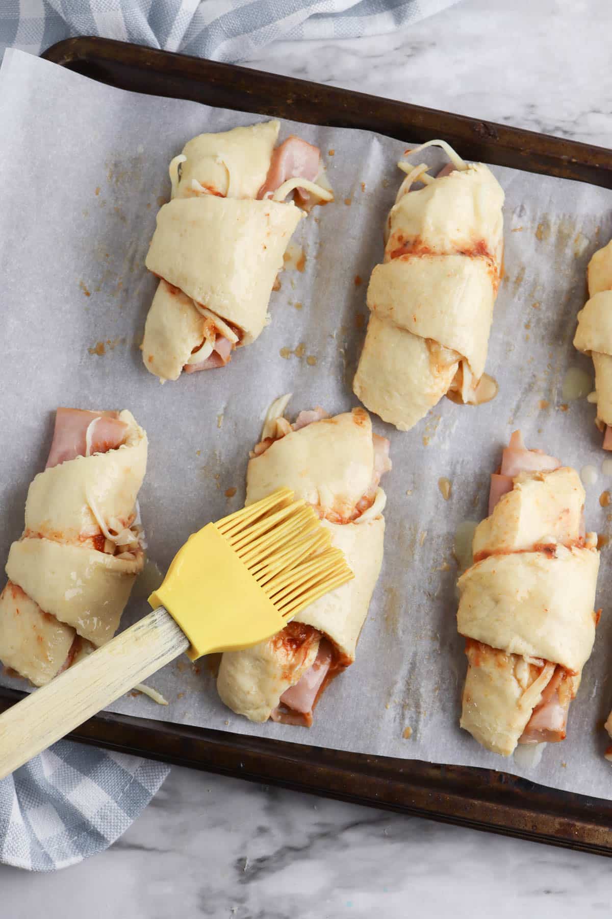 Brushing ham and cheese crescent rolls with butter before baking. 