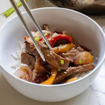 Pepper steak and onions in a white bowl with silver chopsticks.