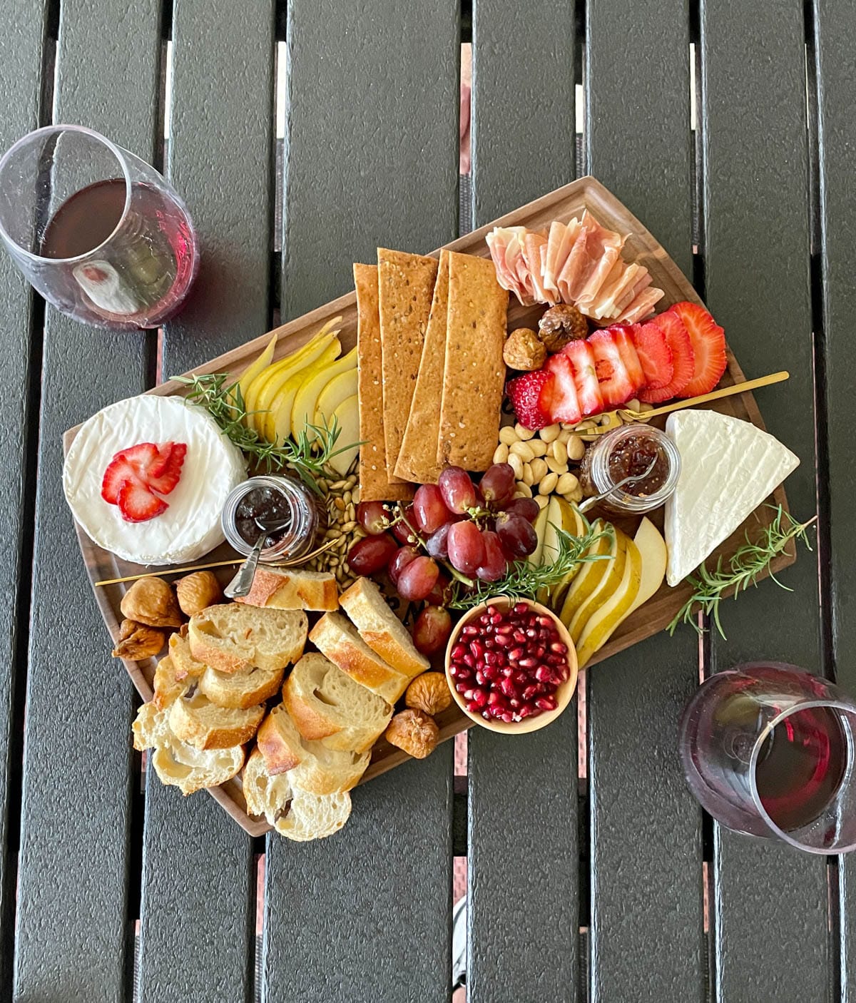 Brie charcuterie board with fruit, nuts, bread, and crackers with glasses of wine.