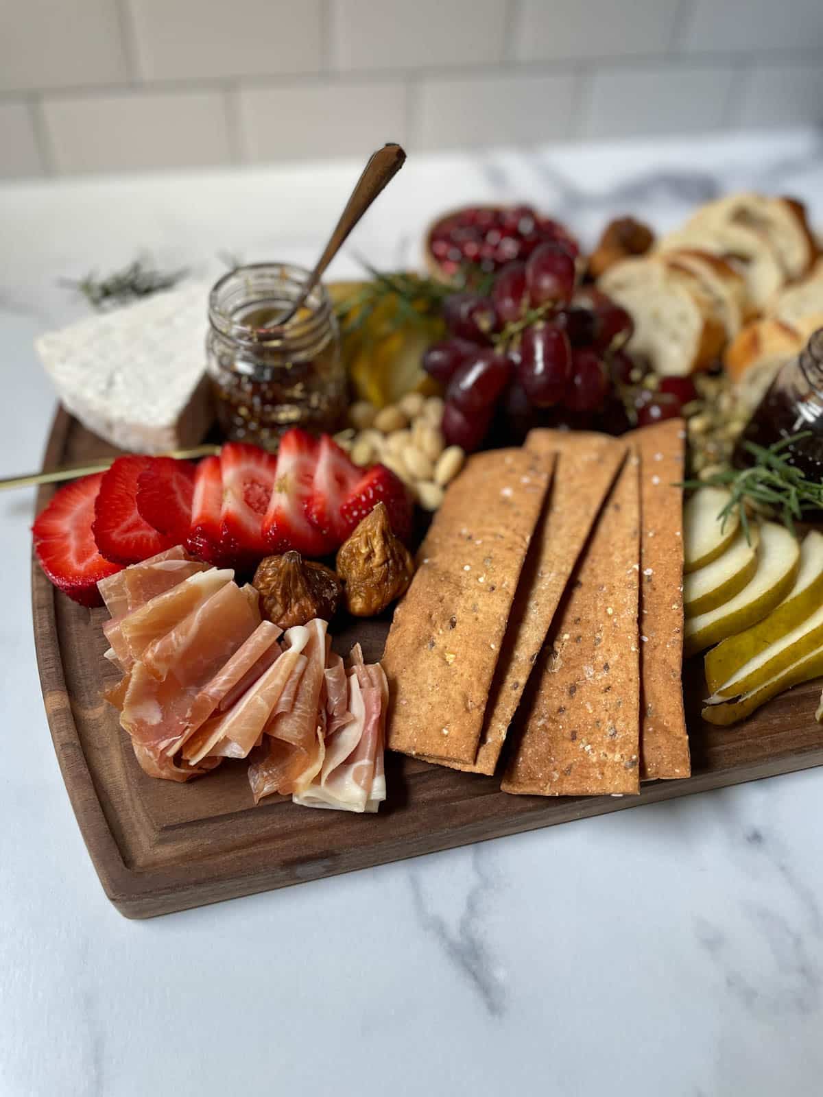 Prosciutto, crackers, strawberry, brie, and fruit on cutting board.