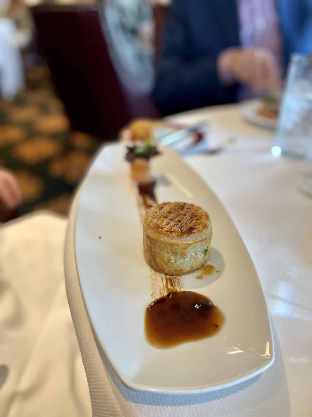 Puff pastry with meat inside and gravy on plate.