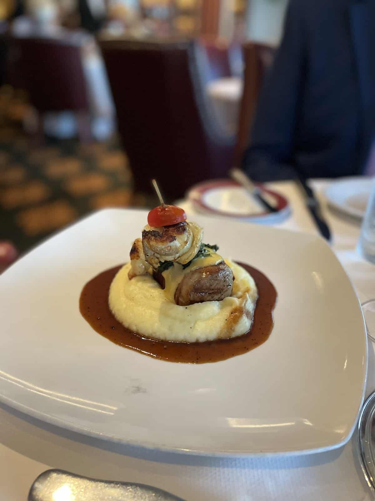 Steak and lobster over mashed potatoes with cherry tomato on top.