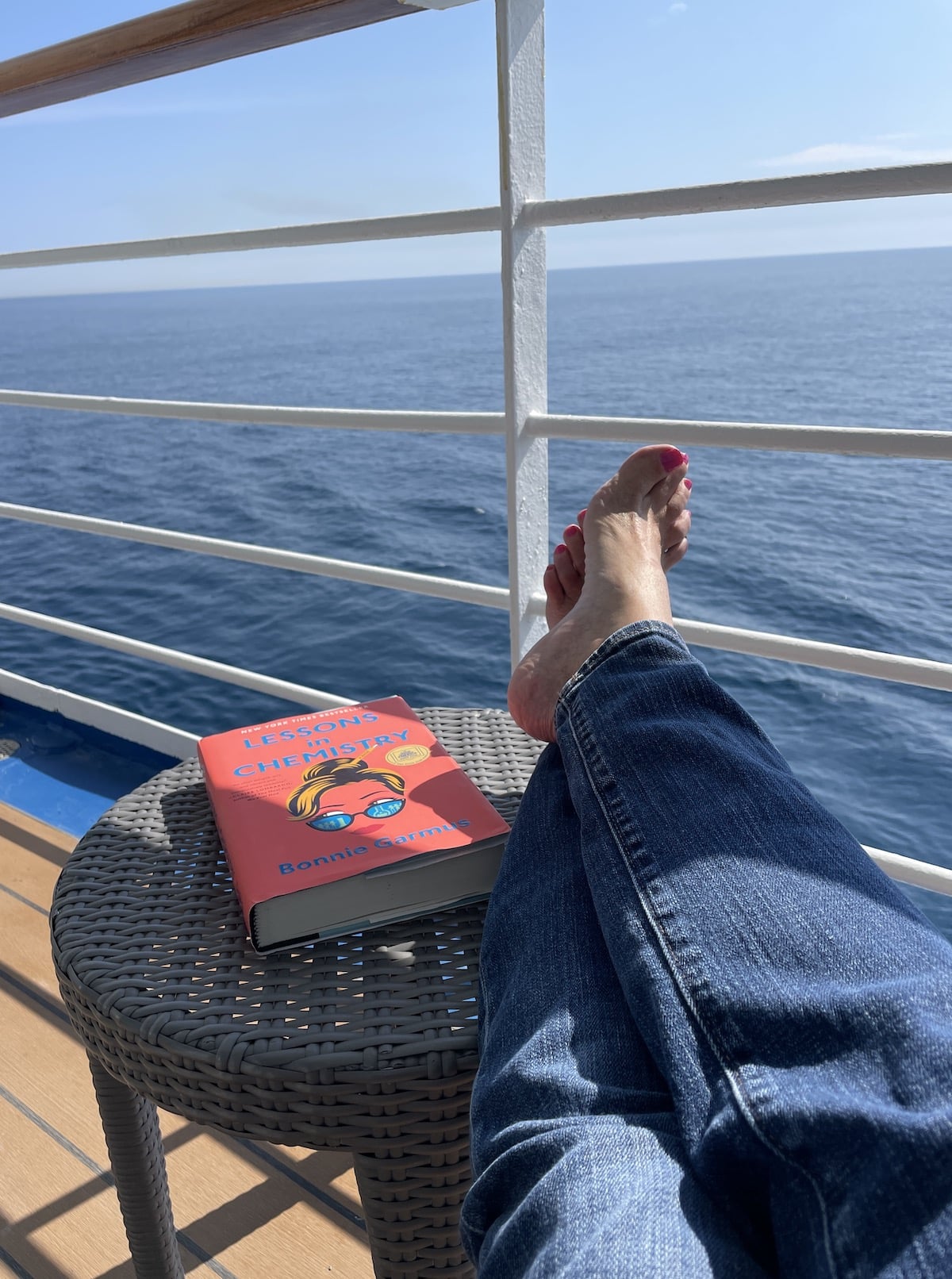 Legs resting on small table with book overlooking sea on cruise ship.
