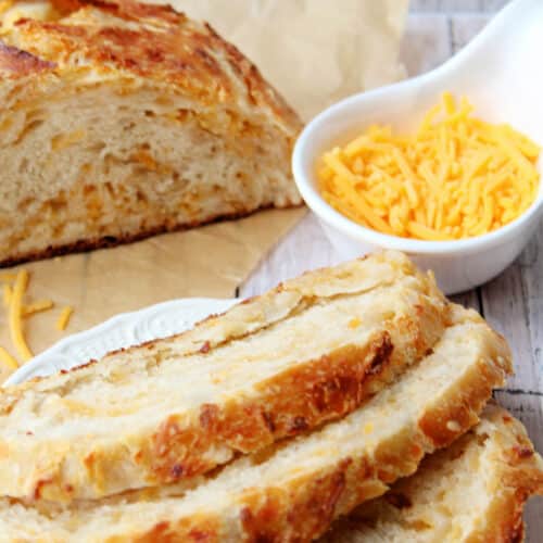 Cheddar bread partially sliced with a bowl of cheddar on side.