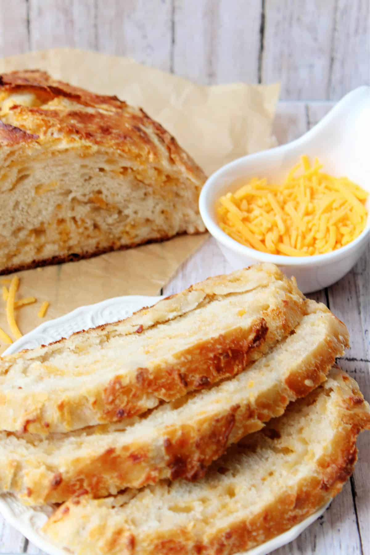 Cheddar bread partially sliced with a bowl of cheddar to the side.