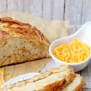 Cheddar bread partially sliced with shredded cheese on side.
